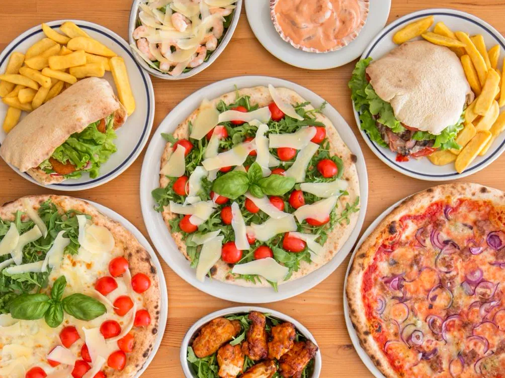 Tavolo pieno di piatti diversi: panini, pizze, alette e gamberetti